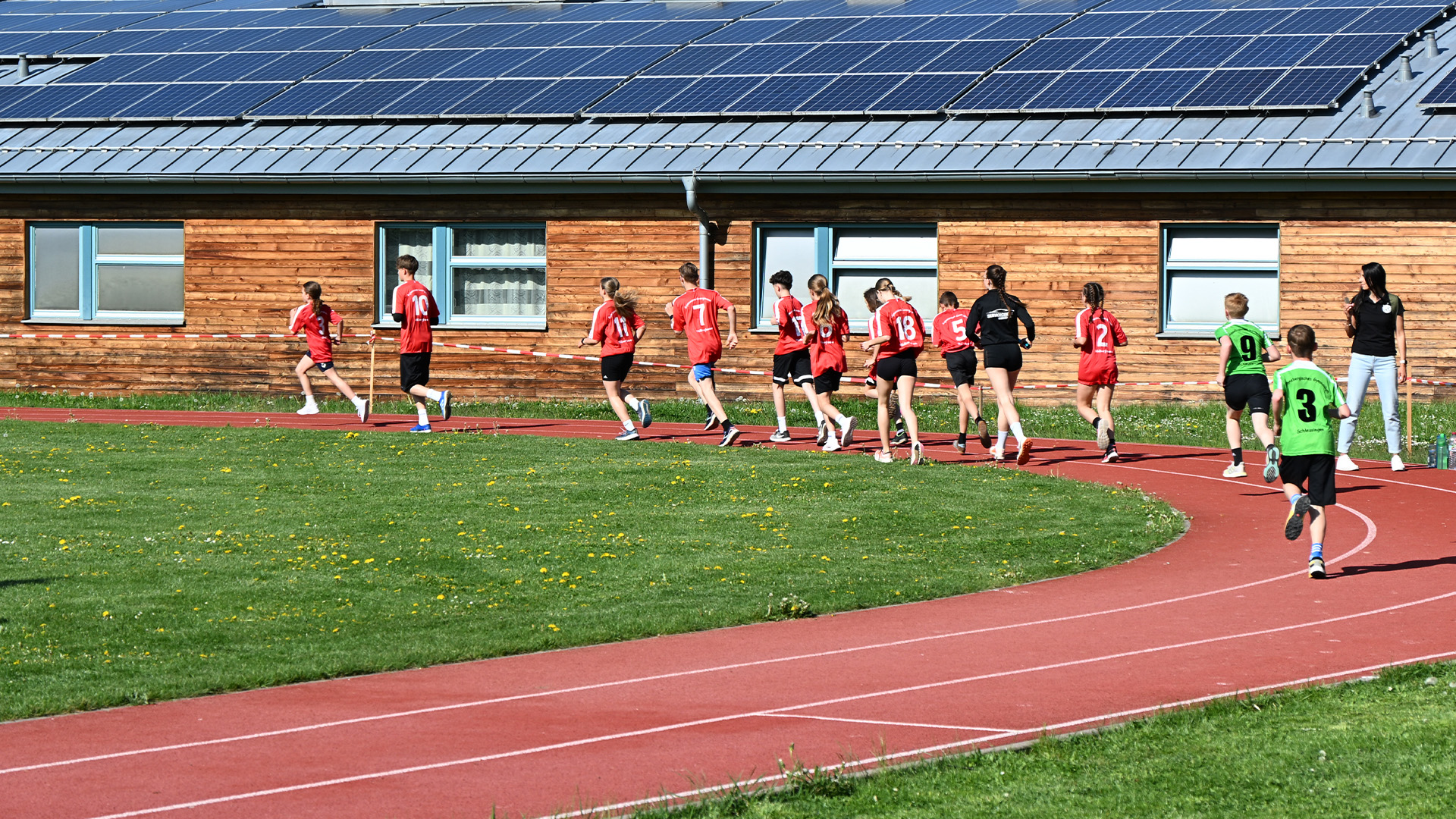 Eine Gruppe junger Sportler in roten und ein grünen Trikots läuft auf einer Laufbahn.