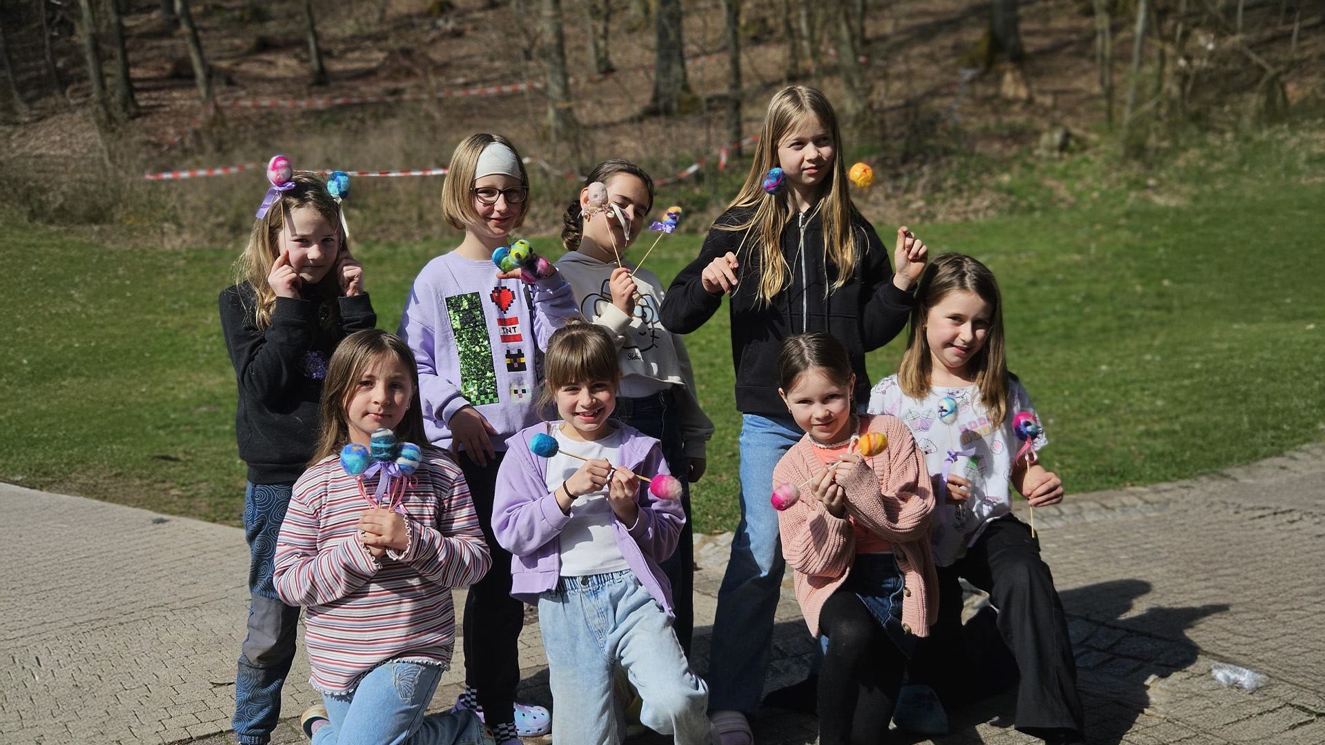 Gruppe von acht Kindern im Freien, lächelnd, mit bunten selbstgemachten Blumen.