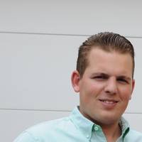 Ein lächelnder Mann mit hellem Hemd und kurzen Haaren vor weißem Hintergrund