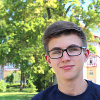 Ein junger Mann mit Brille lächelt vor einem grünen, sonnigen Hintergrund