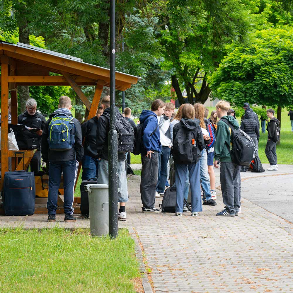 Several teenagers are standing together, looking relaxed, in a green park.