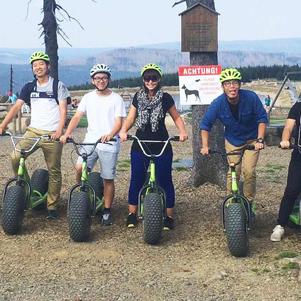 A group of cheerful people wearing green helmets are posing on scooters.