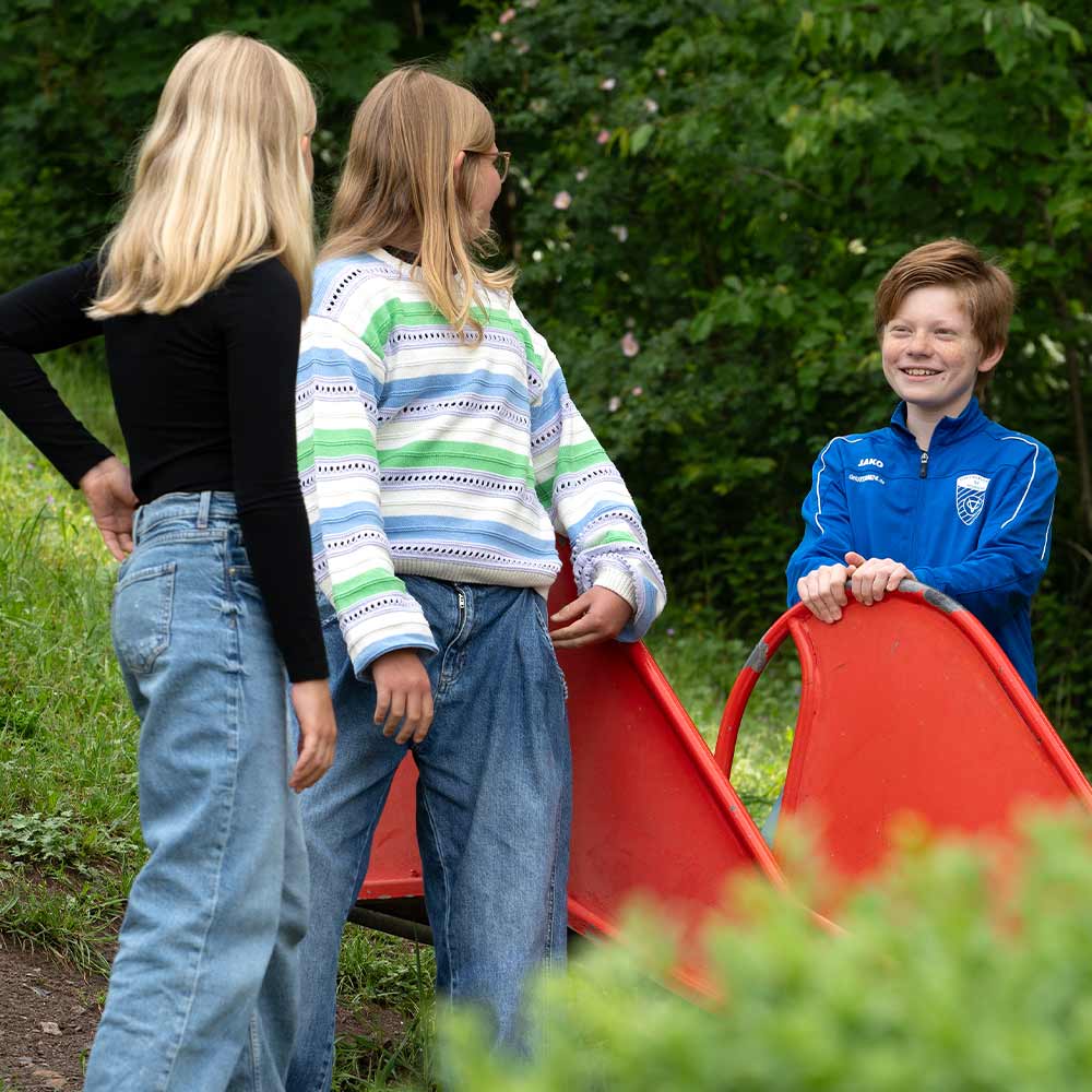 Three children are outside; one is smiling happily, two are wearing glasses, and all are dressed casually.