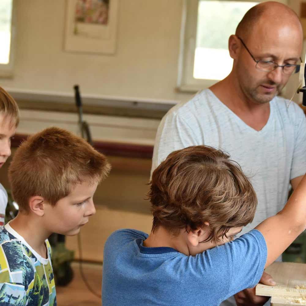 A man in a light gray shirt is showing three children how to operate a machine.