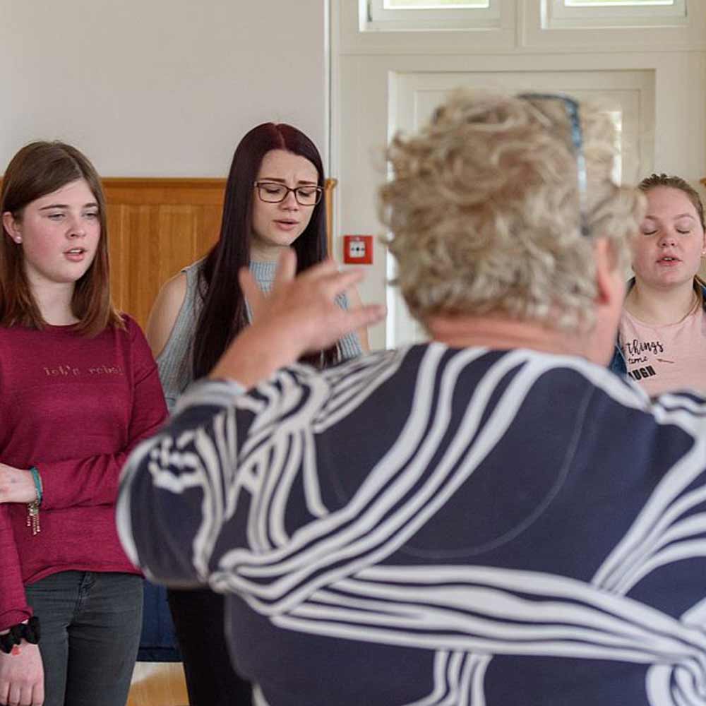 A group of young women is singing while someone conducts them.