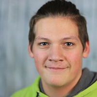 Eine Person mit neutralem Ausdruck trägt einen grünen Hoodie vor grauem Hintergrund