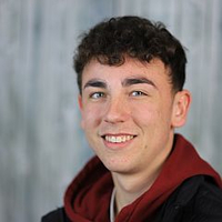 Ein junger Mann lächelt freundlich, trägt eine rot-schwarze Kapuzenjacke.