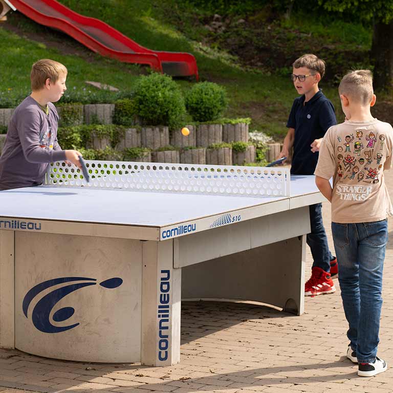 Three boys are happily playing table tennis outdoors on a gray table.