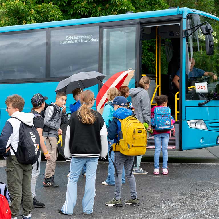 A group of children with colorful backpacks is waiting in front of a blue bus.