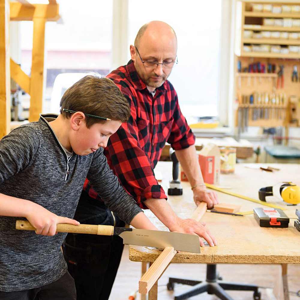 A boy and an older man are working intently in a woodshop.