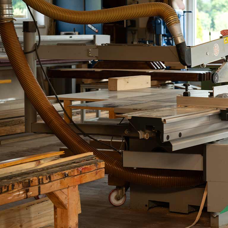 A woodworking shop displays a circular saw with wooden beams in natural light.