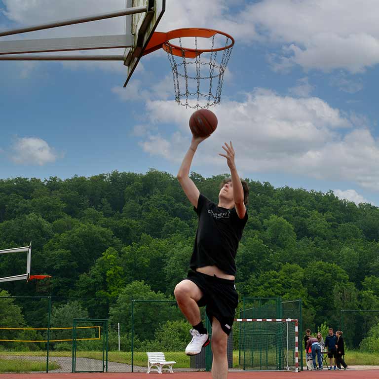 Junger Mann springt in sportlicher Kleidung, um einen Basketball in den Korb zu werfen.