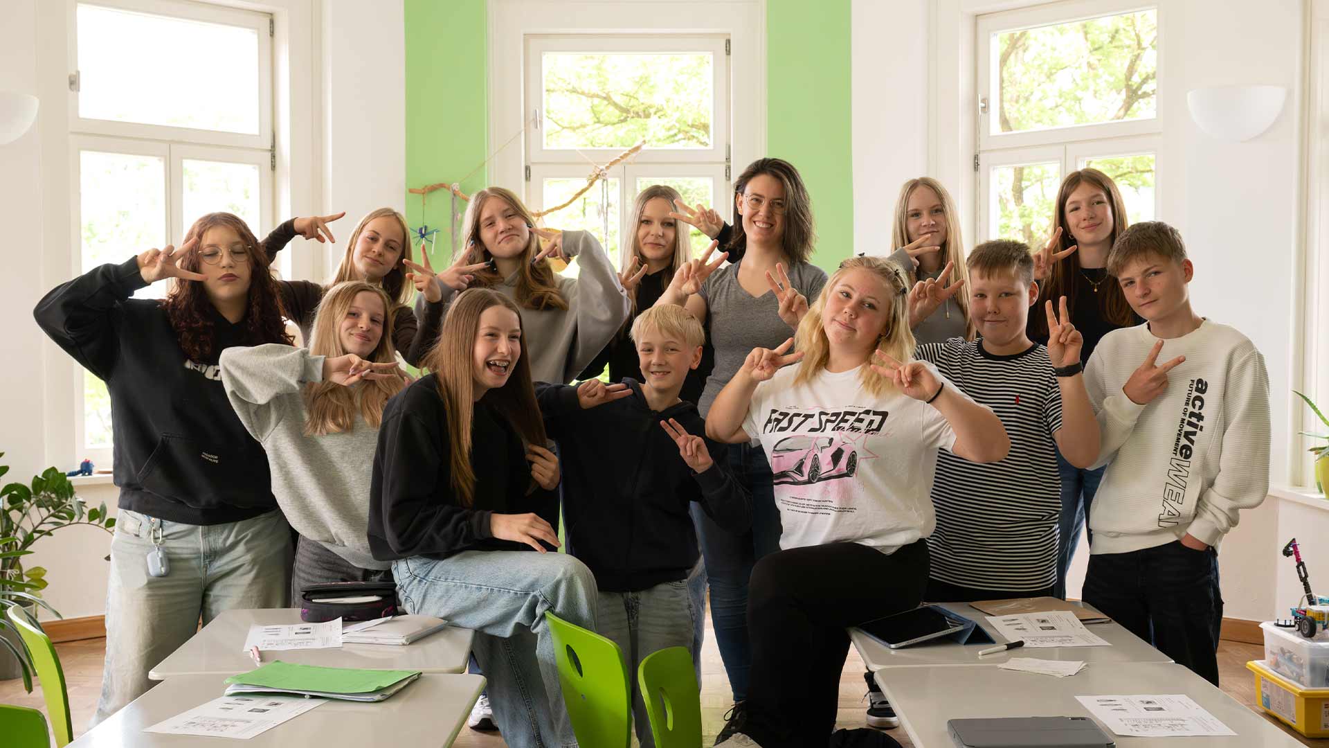 Eine Gruppe junger Menschen posiert fröhlich im Klassenzimmer mit grünen Akzenten