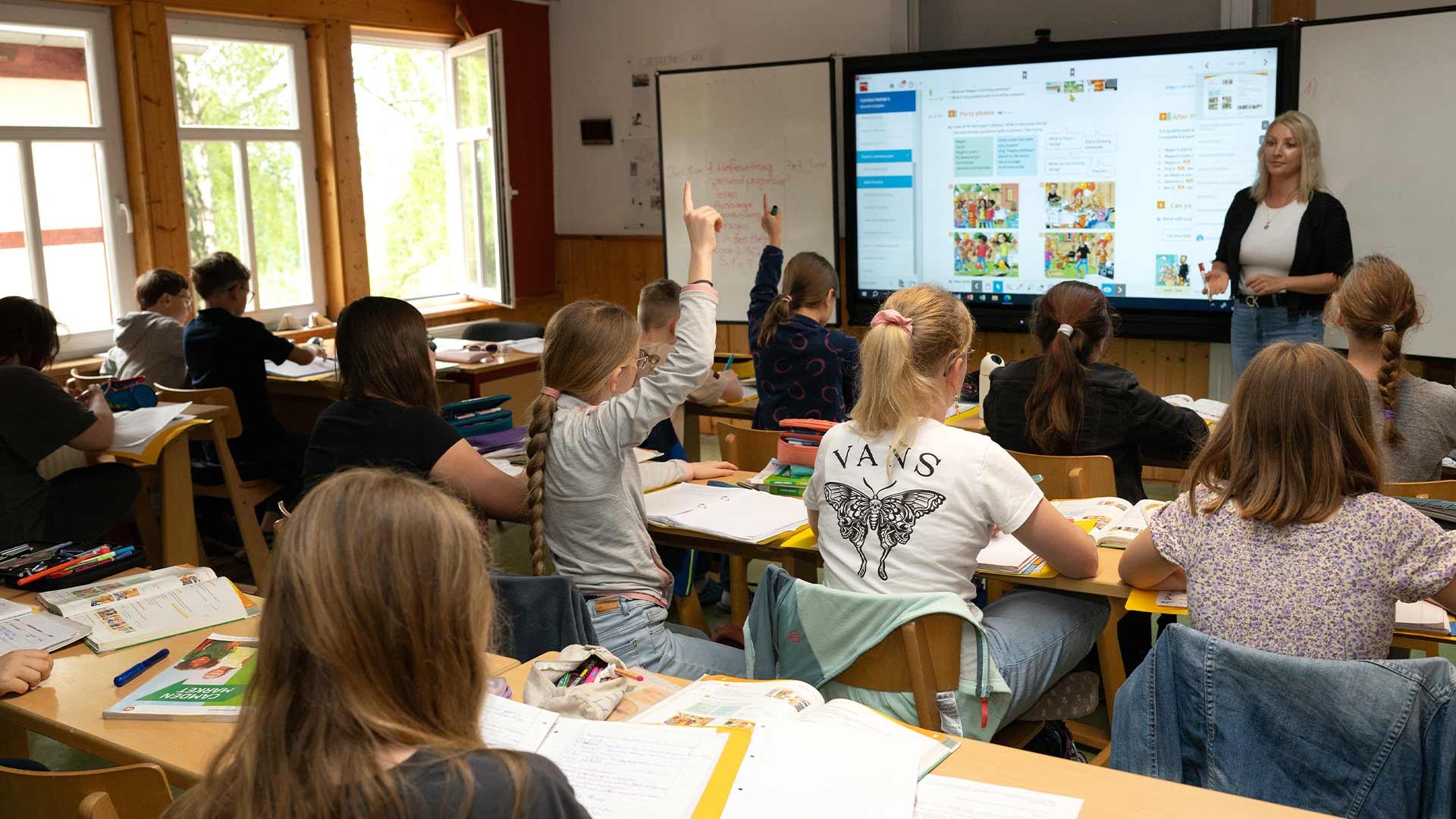 Eine Lehrerin spricht im Klassenzimmer zu aufmerksam schauenden Schülern.
