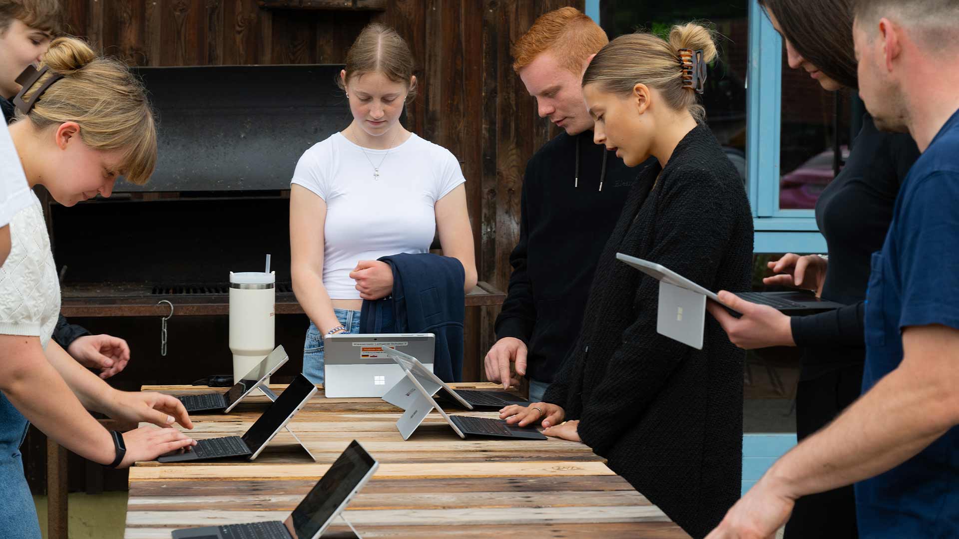 Personen mit konzentrierten Ausdrücken arbeiten an Laptops auf Holztisch im Freien