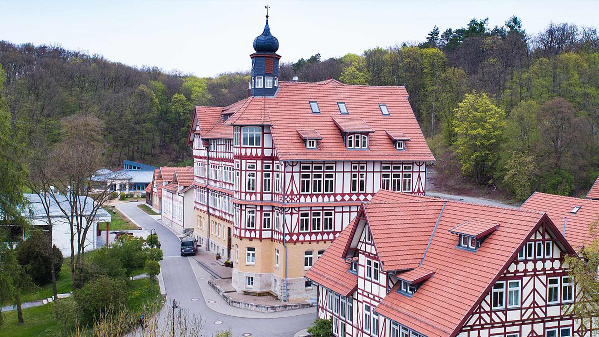 Ein großes, historisches Gebäude mit roten Ziegeldächern und Fachwerkdetails, umgeben von Wald.