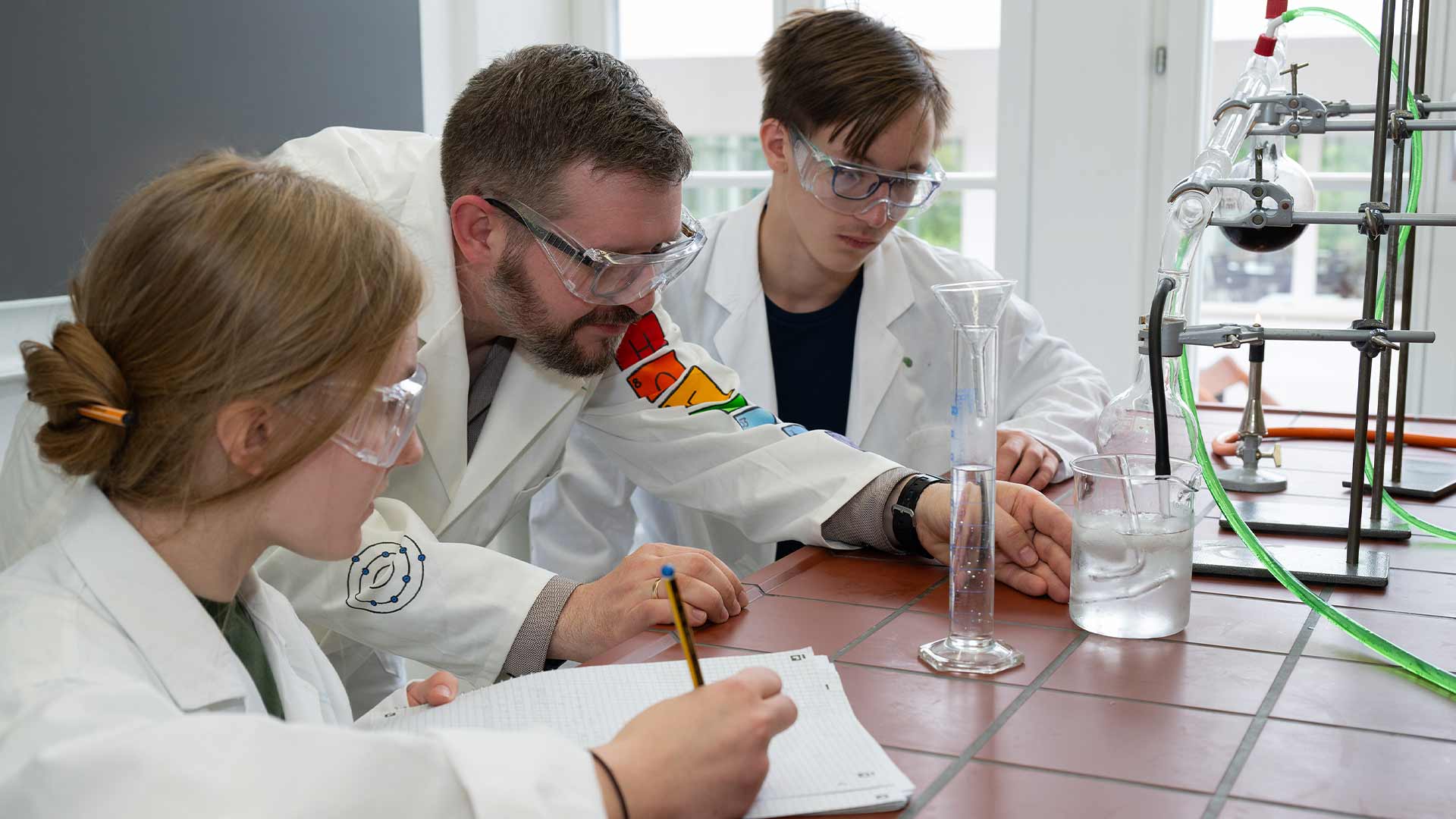 Drei Personen in weißen Kitteln machen ein Chemieexperiment mit Glasgeräten.