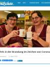 Two smiling women in red shirts are holding white cups in a store