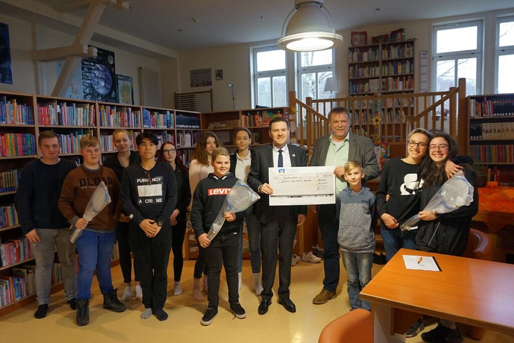 A group of people is standing in a library, holding a large check.