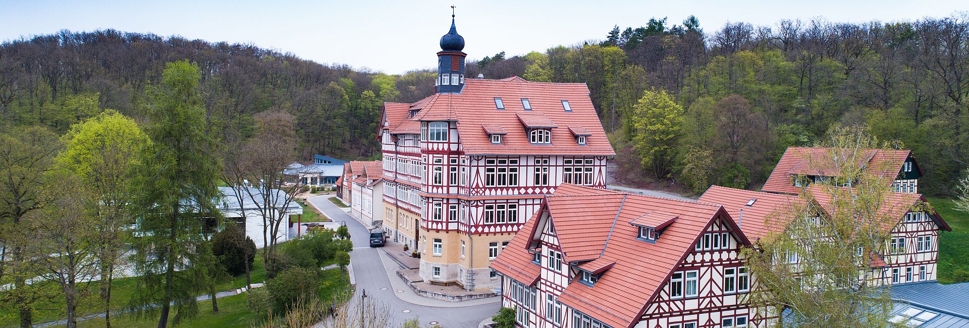 Ein großes Fachwerkhaus mit roten Dächern inmitten grüner Bäume.