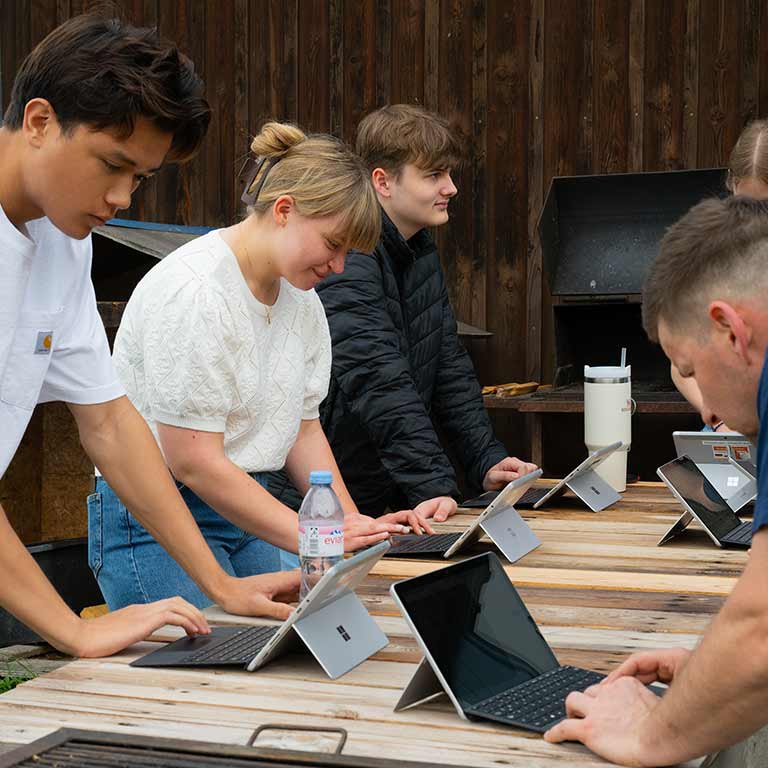 Eine Gruppe junger Menschen konzentriert sich auf Laptops im Freien.