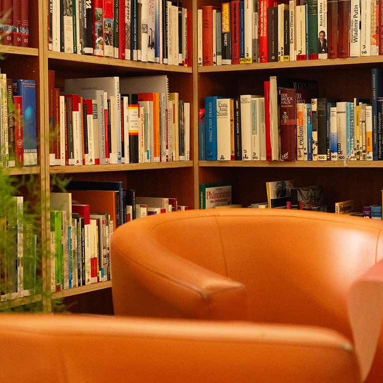 Eine gemütliche Bibliothek mit orangefarbenen Sesseln zwischen vollen Regalen