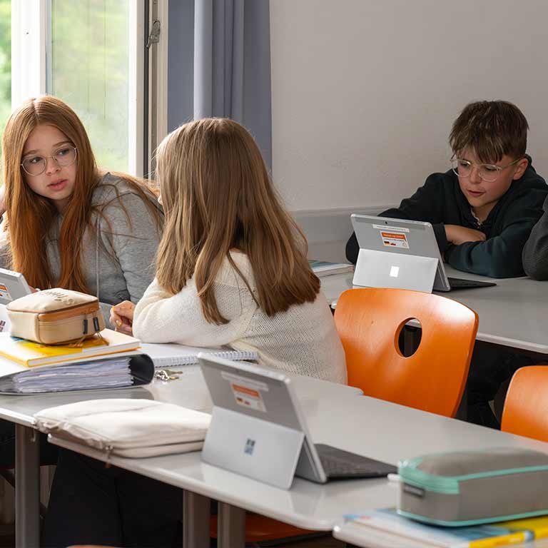 Drei Schüler und Schülerinnen mit Laptops arbeiten aufmerksam im Klassenzimmer.