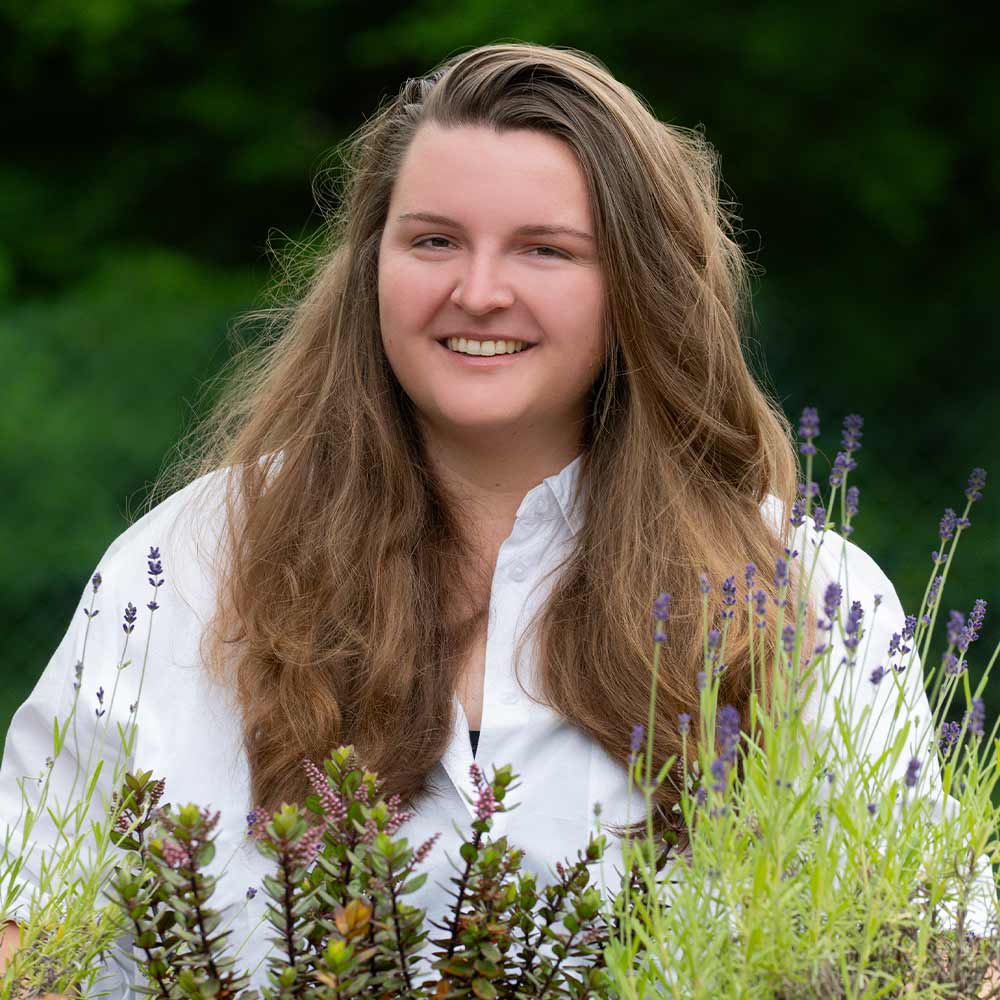 A smiling woman with long brown hair and a white shirt in the garden.