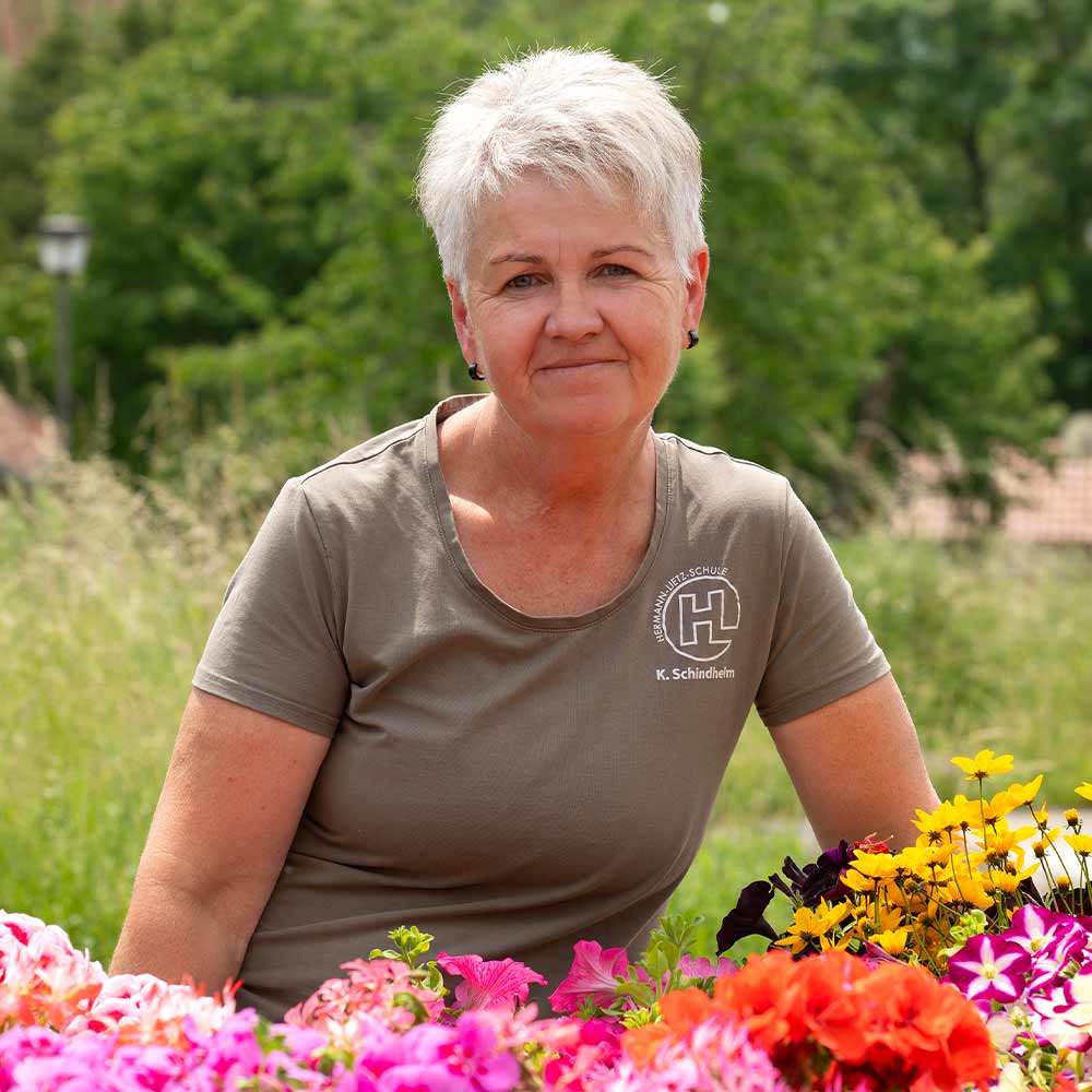 A woman with short gray hair smiles, surrounded by colorful flowers.