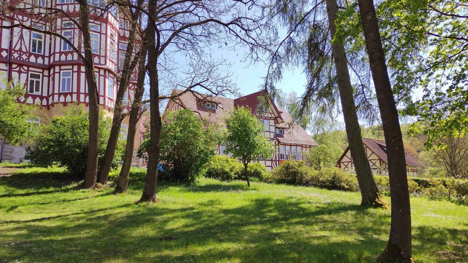 Fachwerkhäuser mit roten Balken stehen im Grünen unter sonnigem Himmel