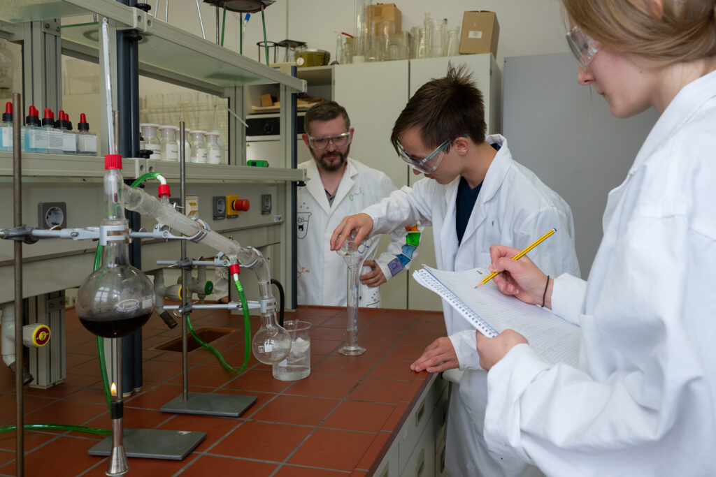 Drei junge Erwachsene in weißen Laborkitteln arbeiten konzentriert im Chemielabor