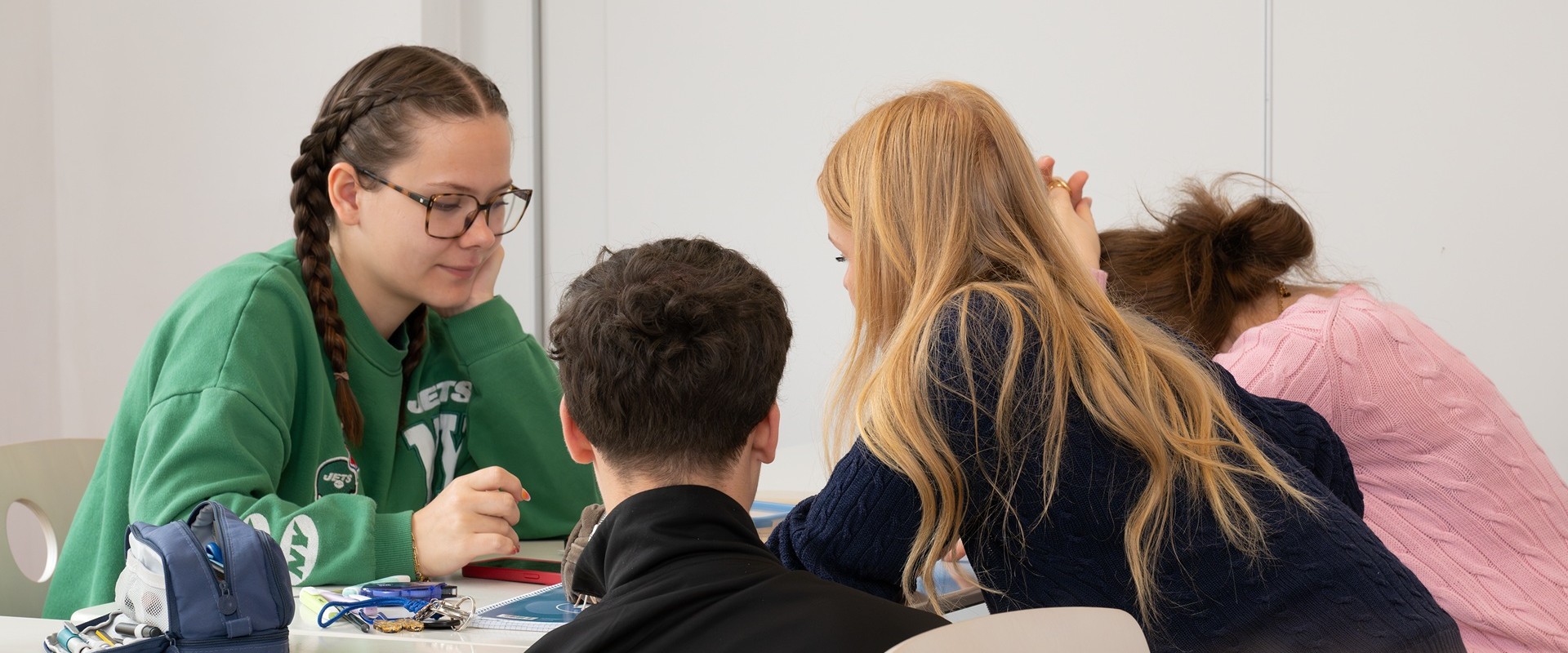 A young woman wearing glasses and a green sweater is chatting amiably with three people at the table