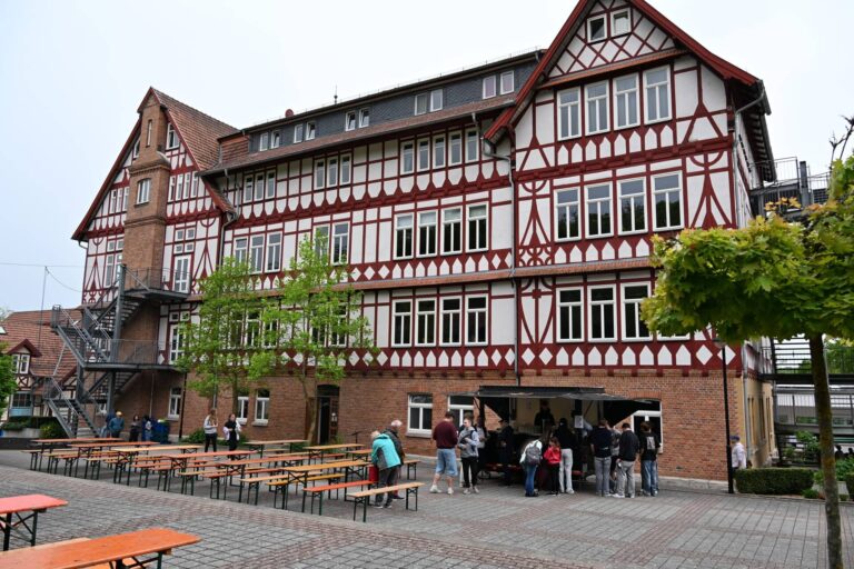 Mehrere Personen stehen und sitzen entspannt vor einem rot-weissen Fachwerkgebäude