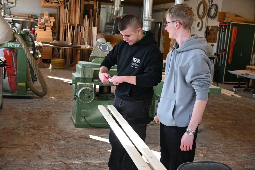 Zwei junge Männer schneiden Holzbretter in einer Werkstatt und wirken konzentriert