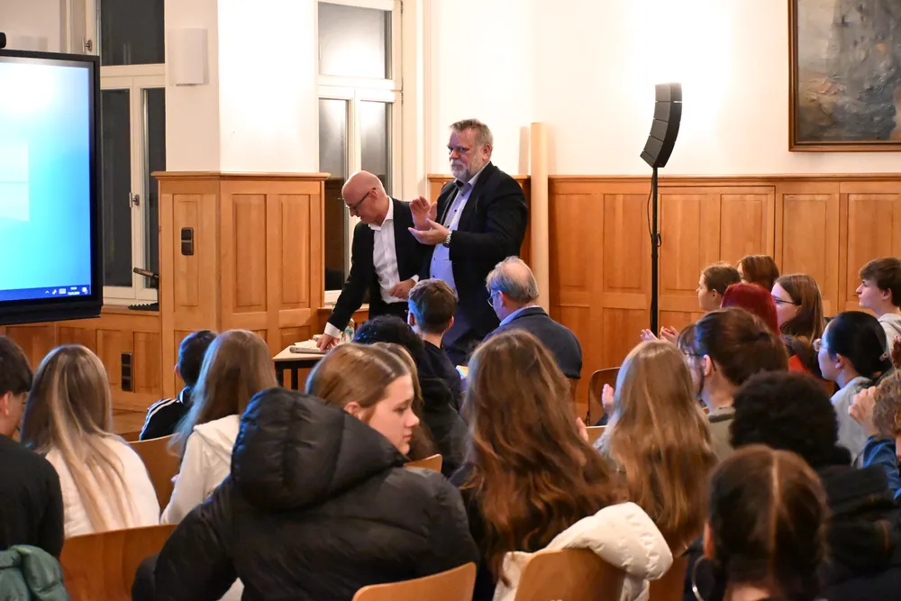 Ein älterer Mann im Anzug spricht lebhaft vor einer Gruppe von aufmerksamem Publikum