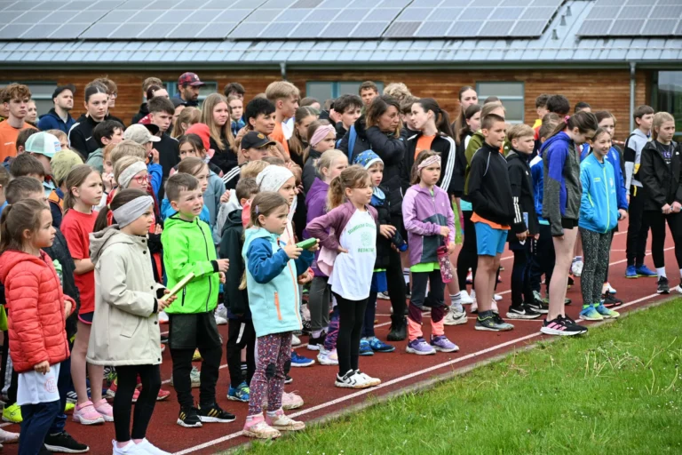 Eine große Gruppe von Kindern und Jugendlichen steht erwartungsvoll auf einer Laufbahn