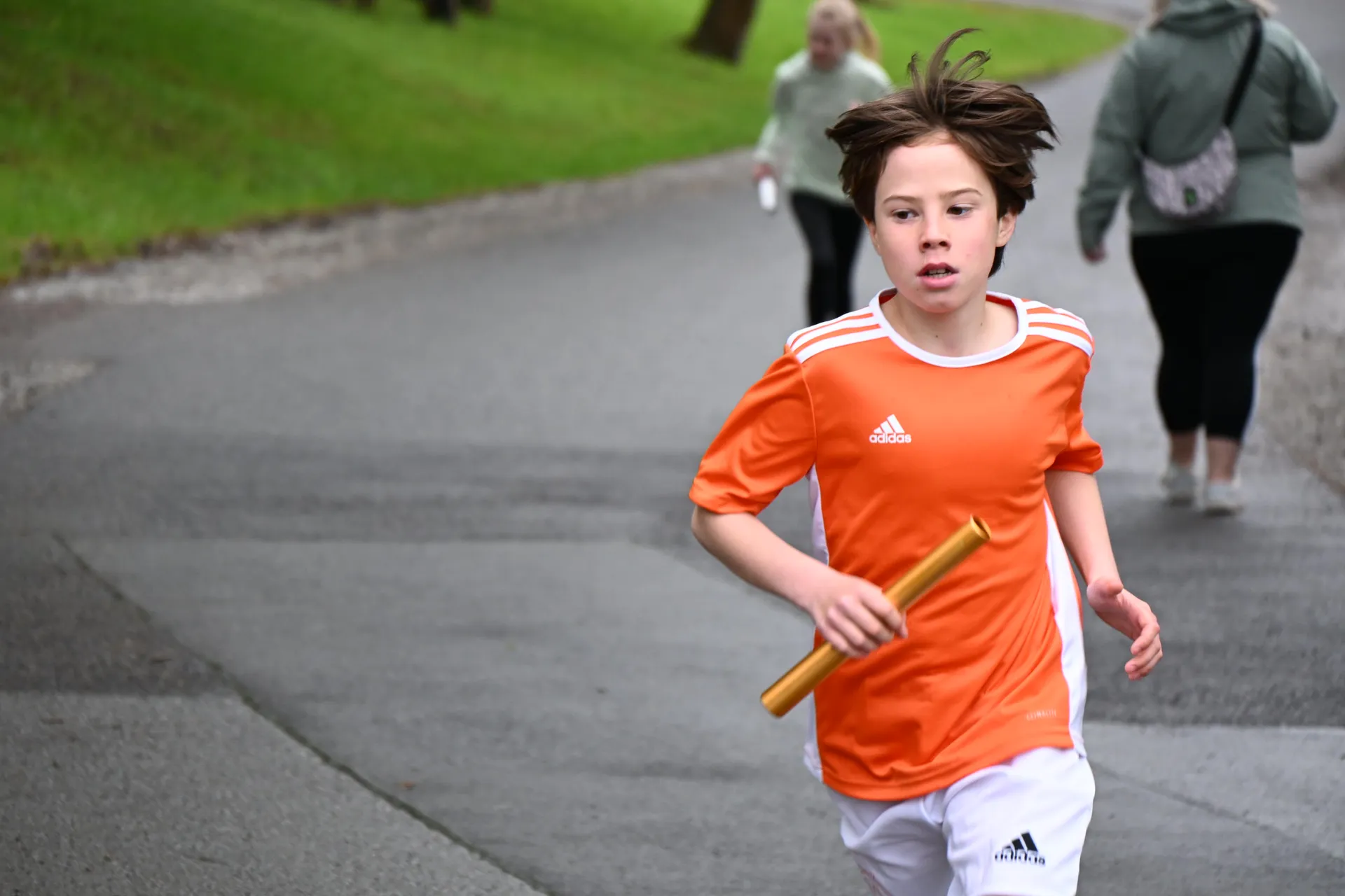 Ein Junge mit fröhlichem Gesichtsausdruck läuft in orangefarbenem Trikot mit einem Staffelstab