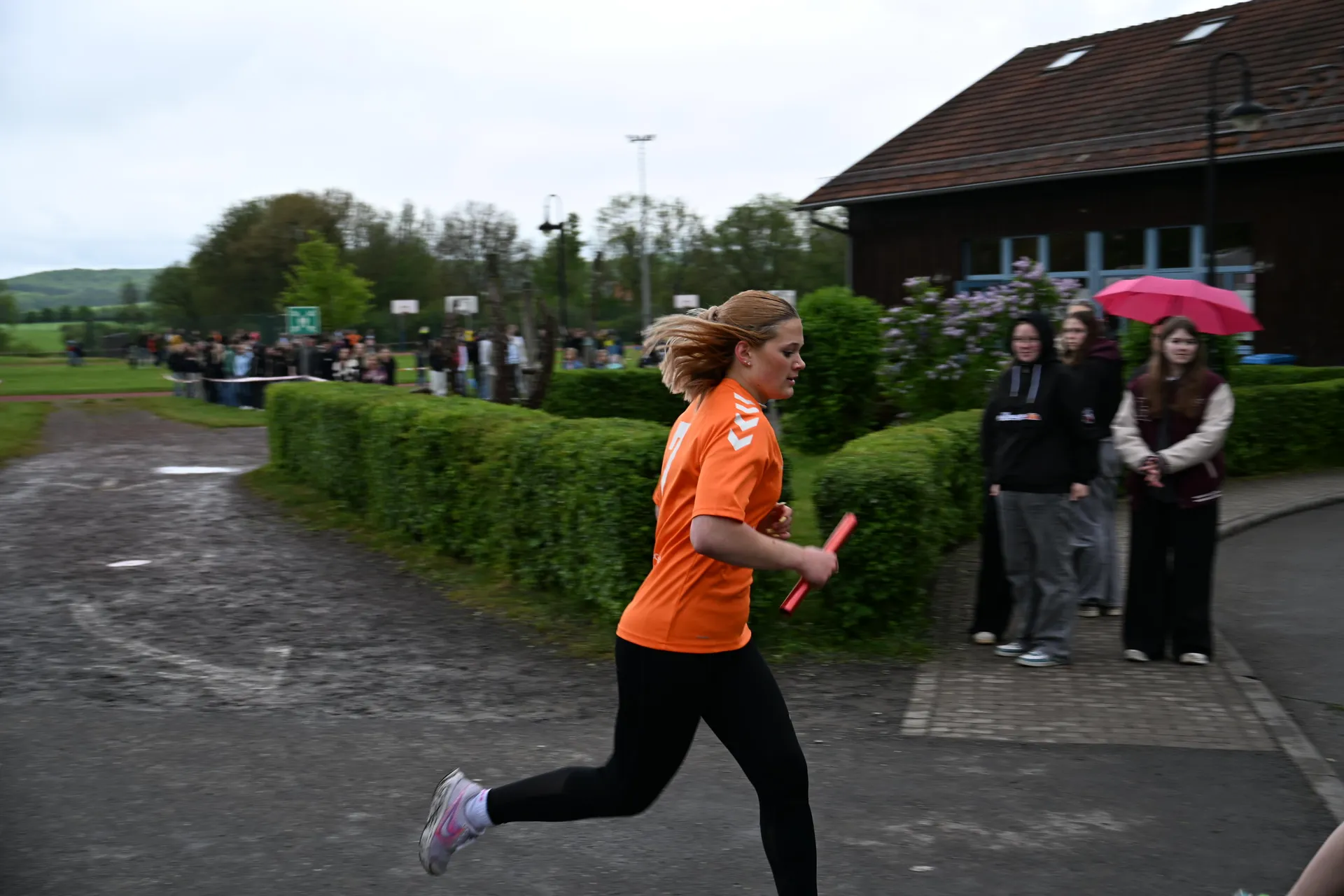 Eine junge Frau läuft mit entschlossenem Blick im orangefarbenen Trikot und hält einen Staffelstab