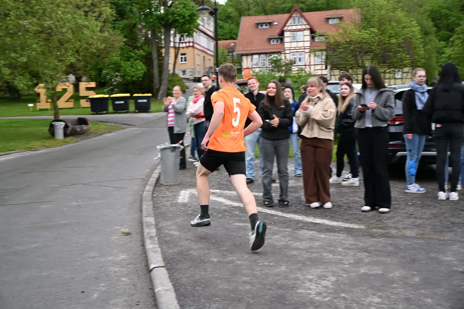 Ein junger Mann in orangefarbenem Trikot läuft lachend vor jubelnden Zuschauern