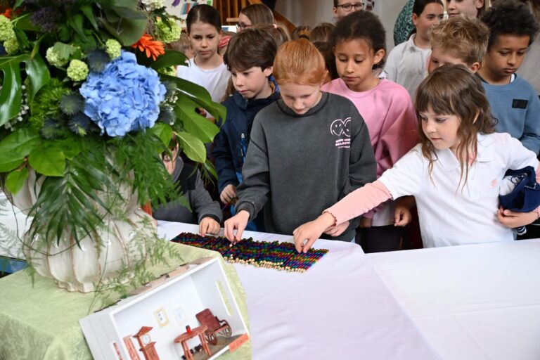 Eine Gruppe Kinder betrachtet konzentriert bunte Legosteine auf einem weißen Tisch