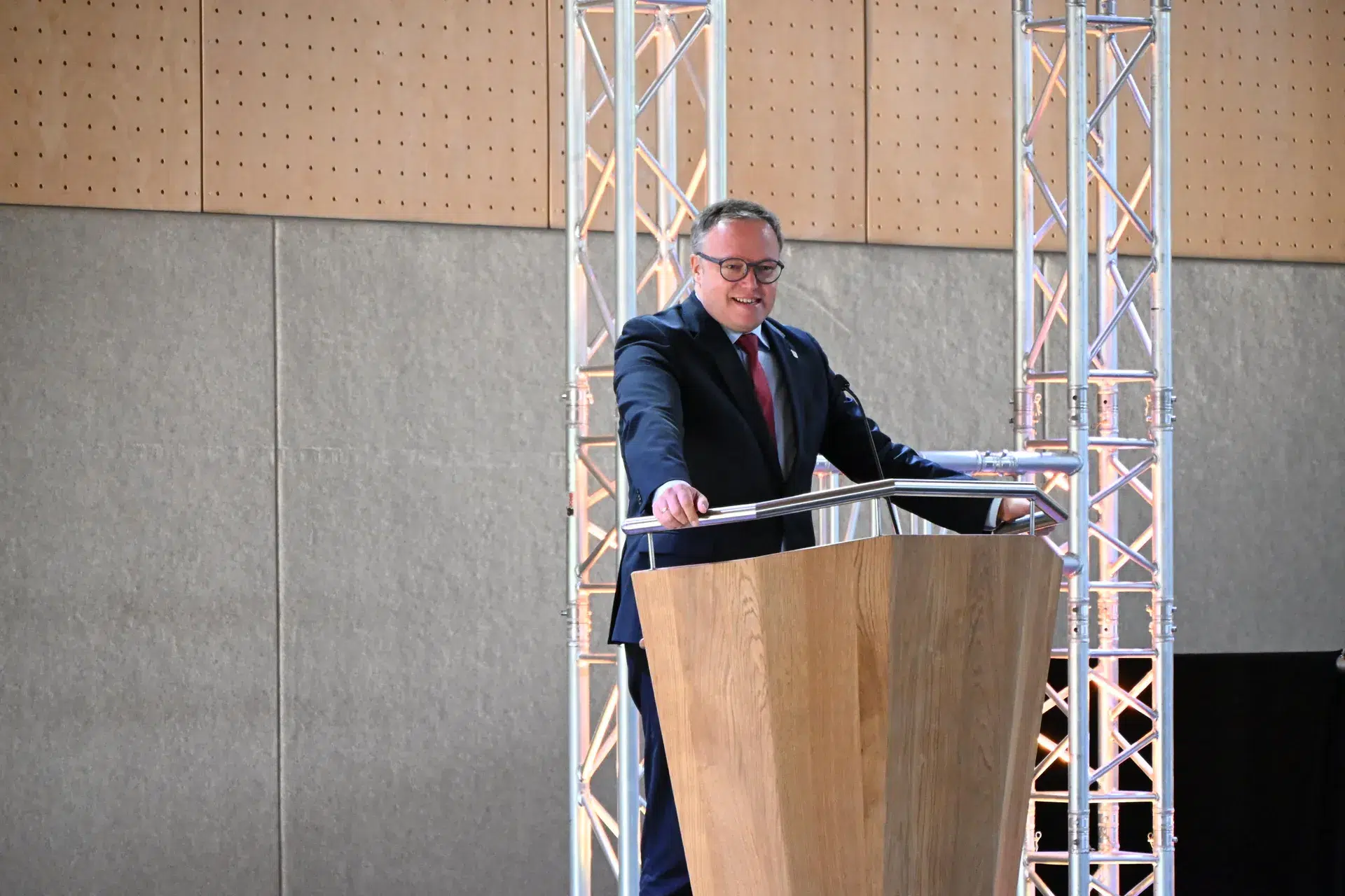 Ein Mann im dunklen Anzug spricht ernst an einem Holzpodium vor Metallstreben