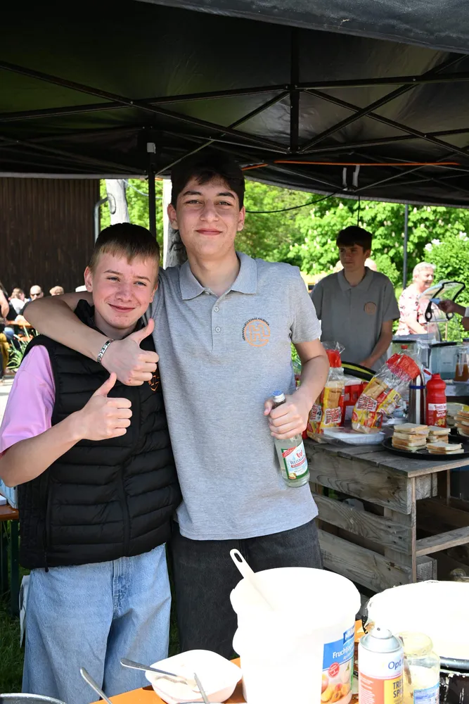 Zwei junge Männer lächeln freundlich, einer hält eine Flasche, beide tragen Freizeitkleidung