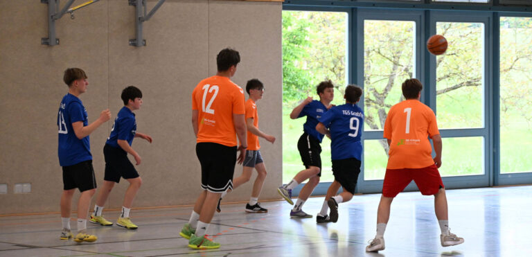 Jugendliche spielen Basketball in Blau und Orange mit konzentriertem Blick