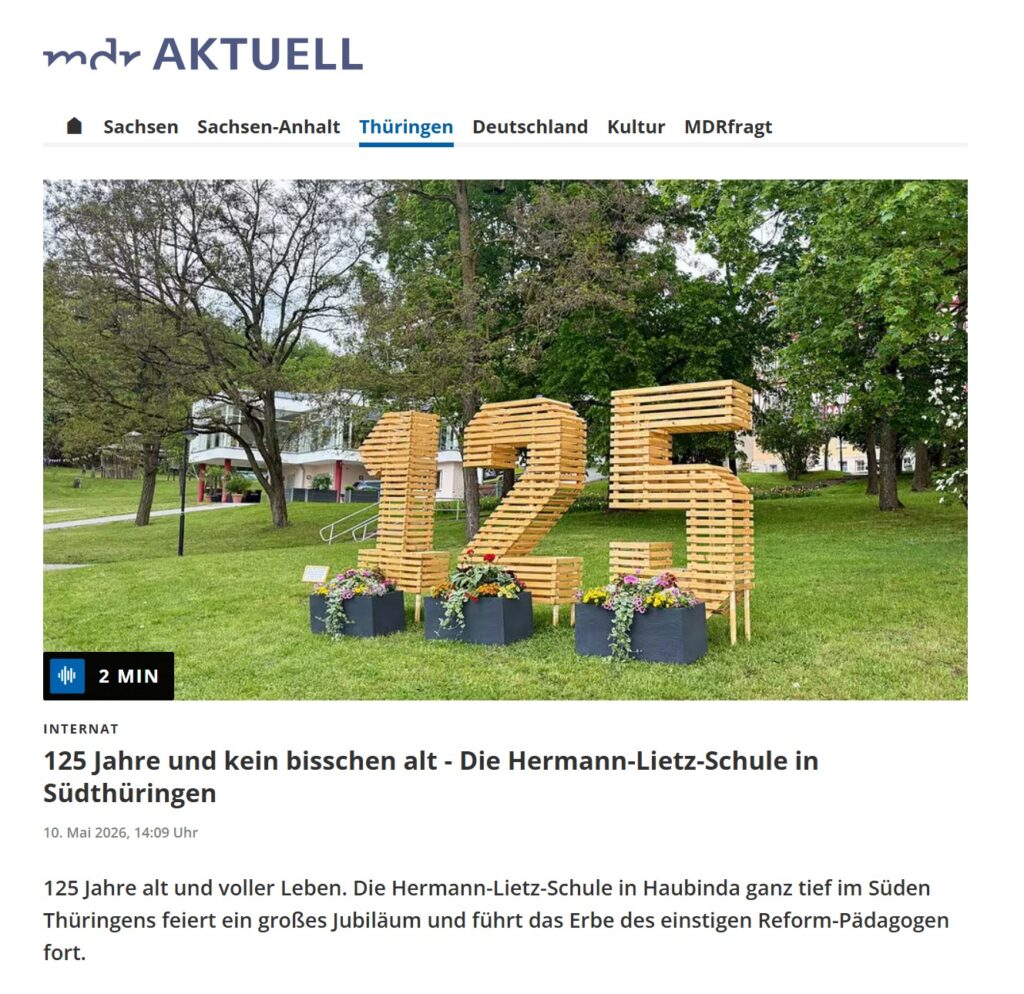 Eine große goldene 125 aus Holz steht neben Bäumen auf einer grünen Wiese