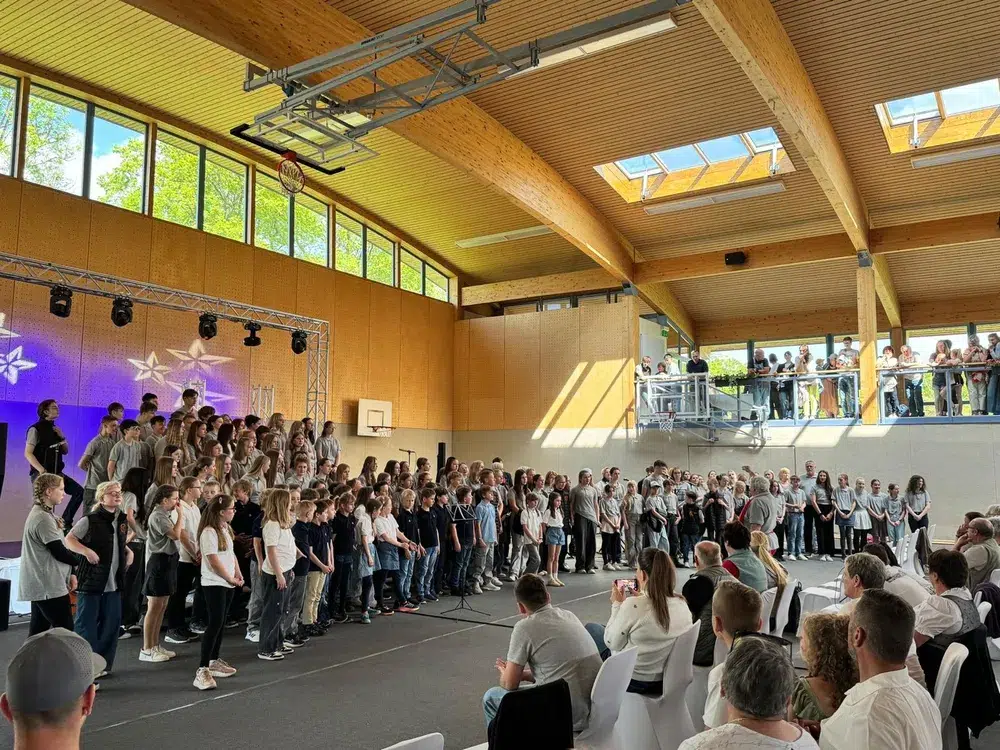 Eine große Gruppe junger Menschen steht lächelnd auf einer Bühne in heller Kleidung