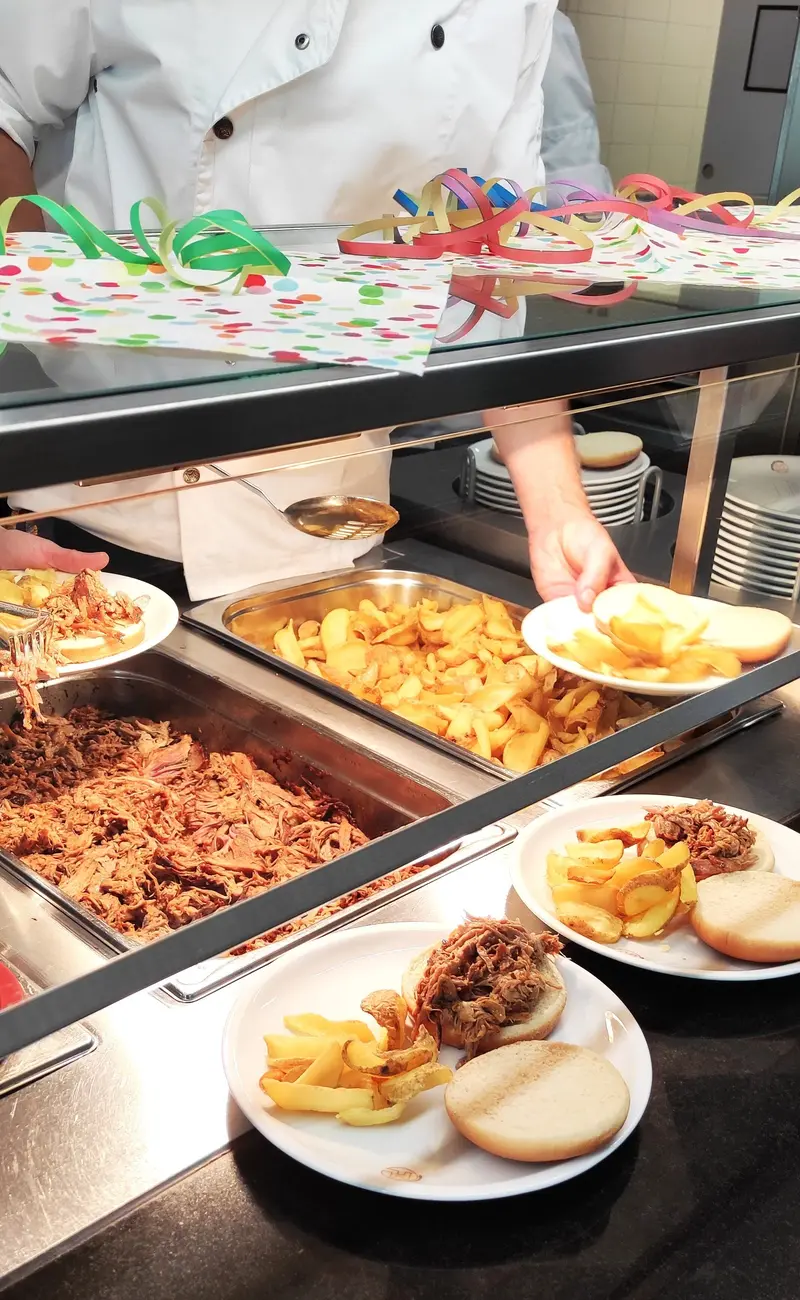 Koch in weisser Jacke mit konzentriertem Blick richtet Pommes am Buffet mit bunten Girlanden an