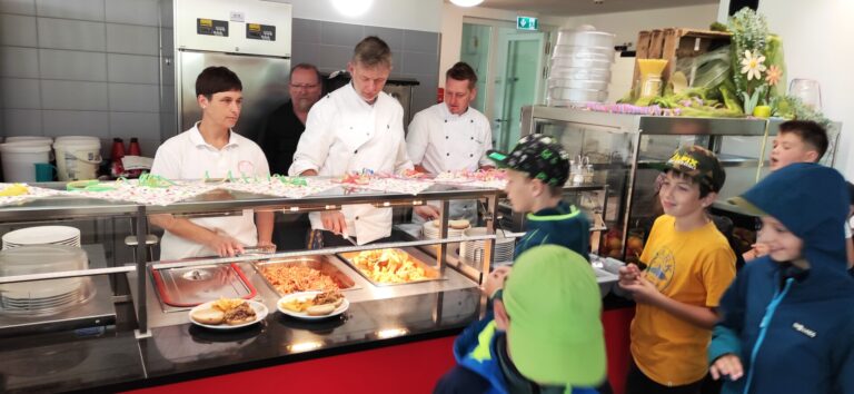 Mehrere Köche mit neutralem Blick servieren buntes Buffet im Rotton