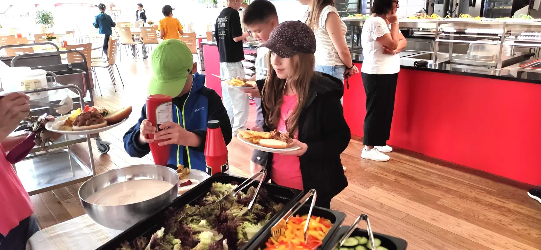 Zwei Personen mit neutralem Blick am Buffet mit bunten Speisen und Rottoenen