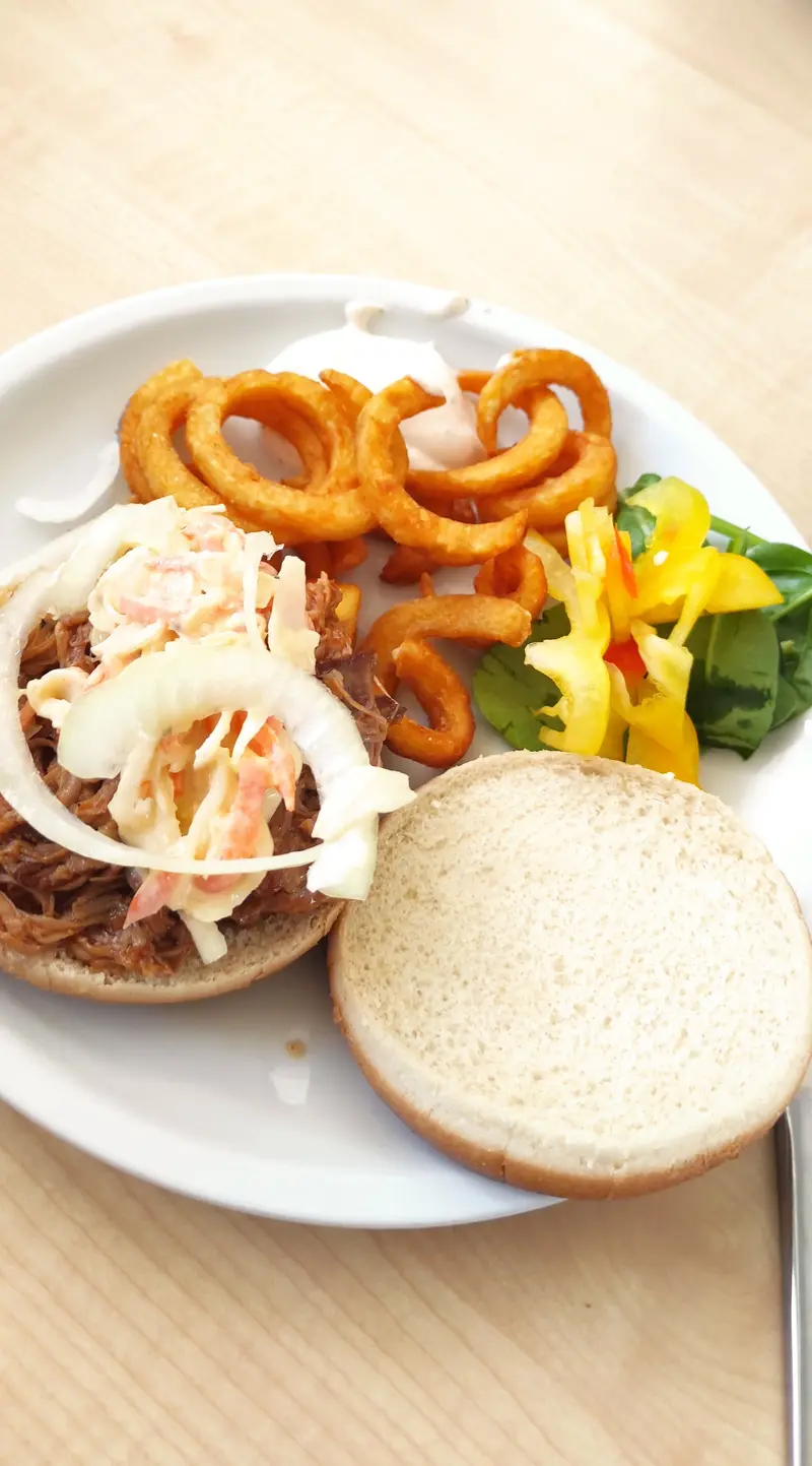 Burger mit Pulled Pork, Krautsalat, Zwiebel, Curly Fries und Salatbeilage in Beige und Orange, appetitlich angerichtet