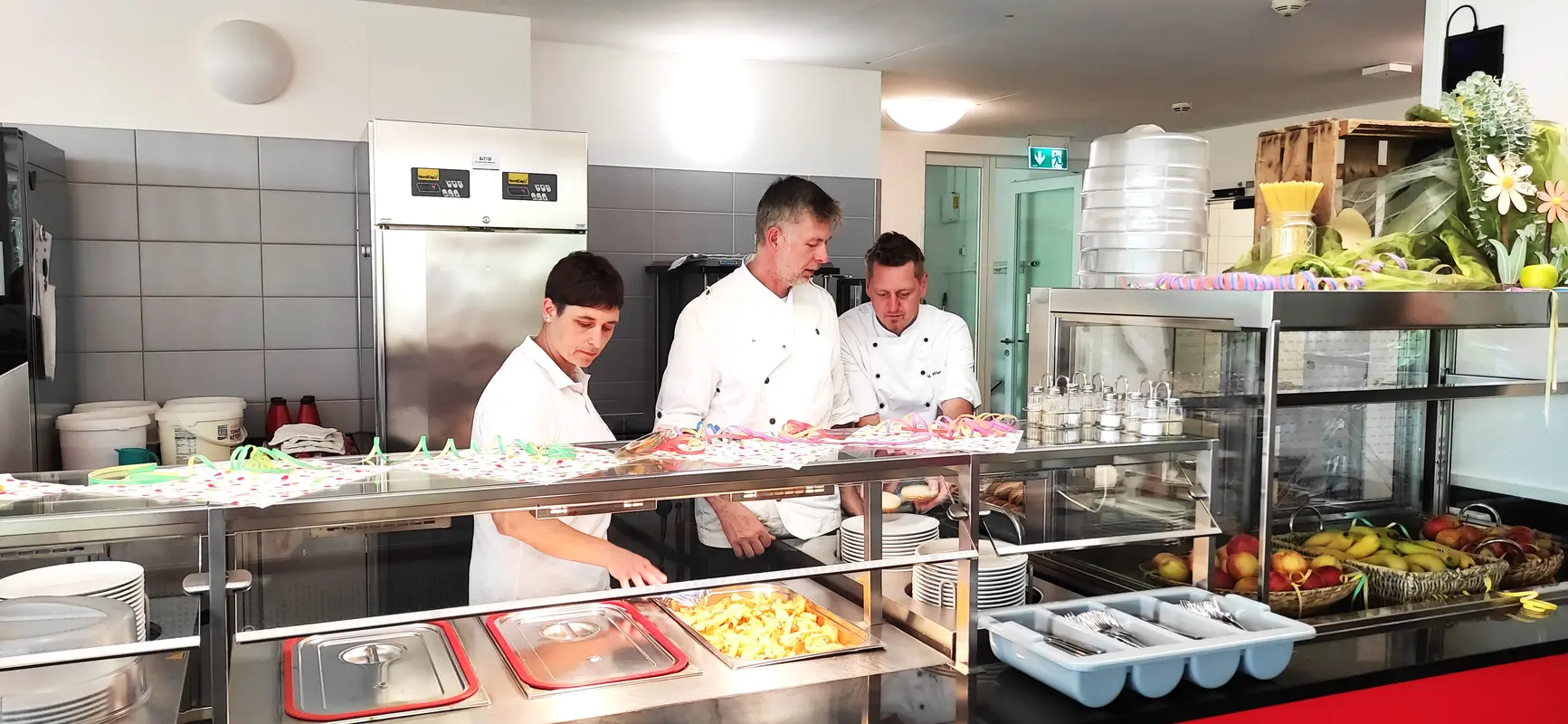 Drei Köche mit neutralem Blick in weißer Küche am Buffet mit Obst